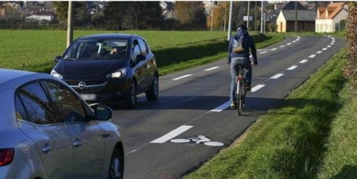 Une route avec un cycliste sur piste cyclable, et deux voitures
