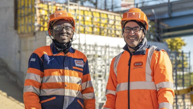 2 hommes avec des vestes oranges de chantier et des casques oranges