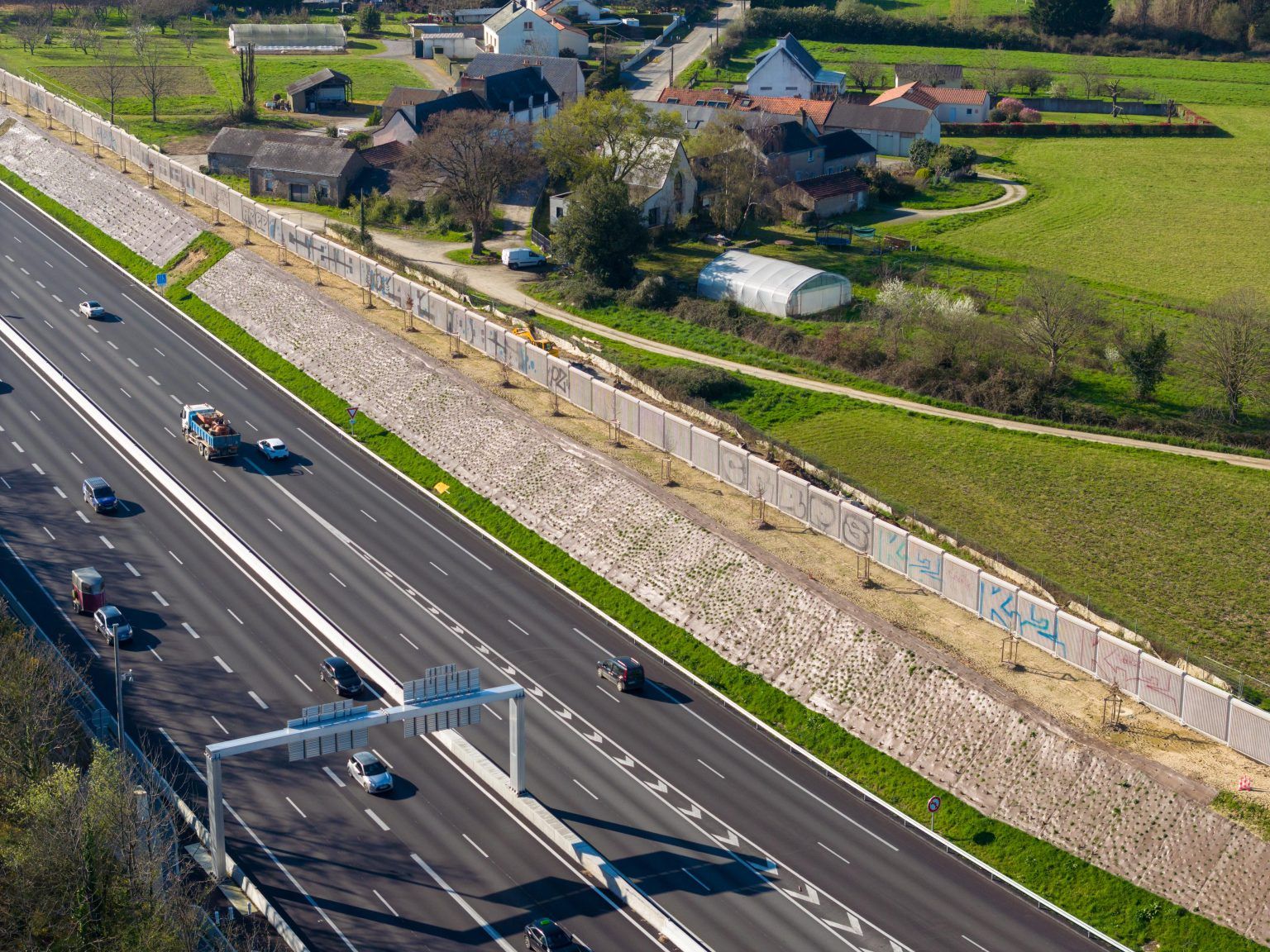 Photo vue du ciel de l'autoroute A11. Des maisons se trouvent aux abords de l'autoroute, et des murs acoustiques se dressent entre les deux pour protéger les riverains des nuisances sonores.